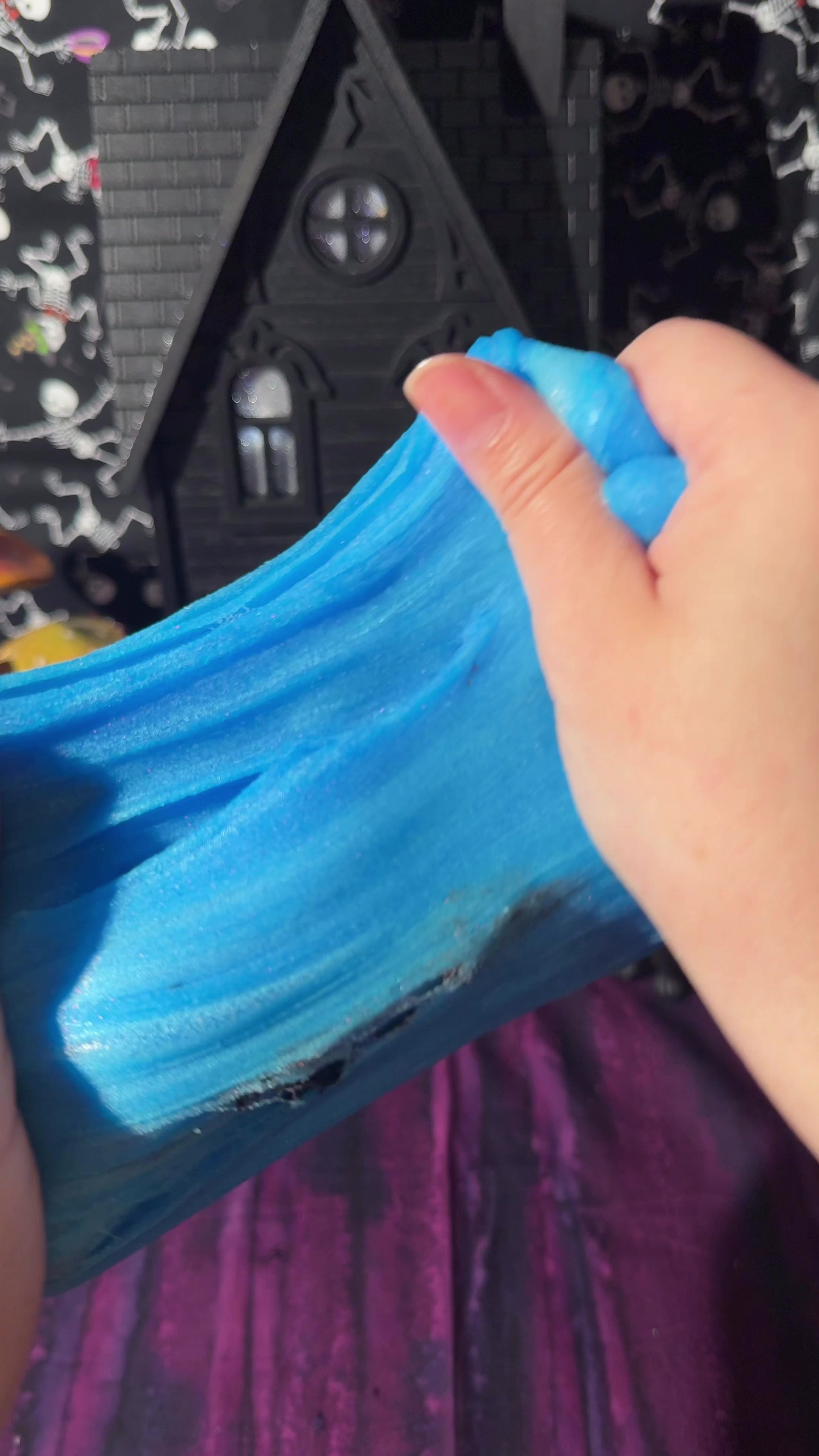 hands stretching iridescent blue icee slime in a texture demo video